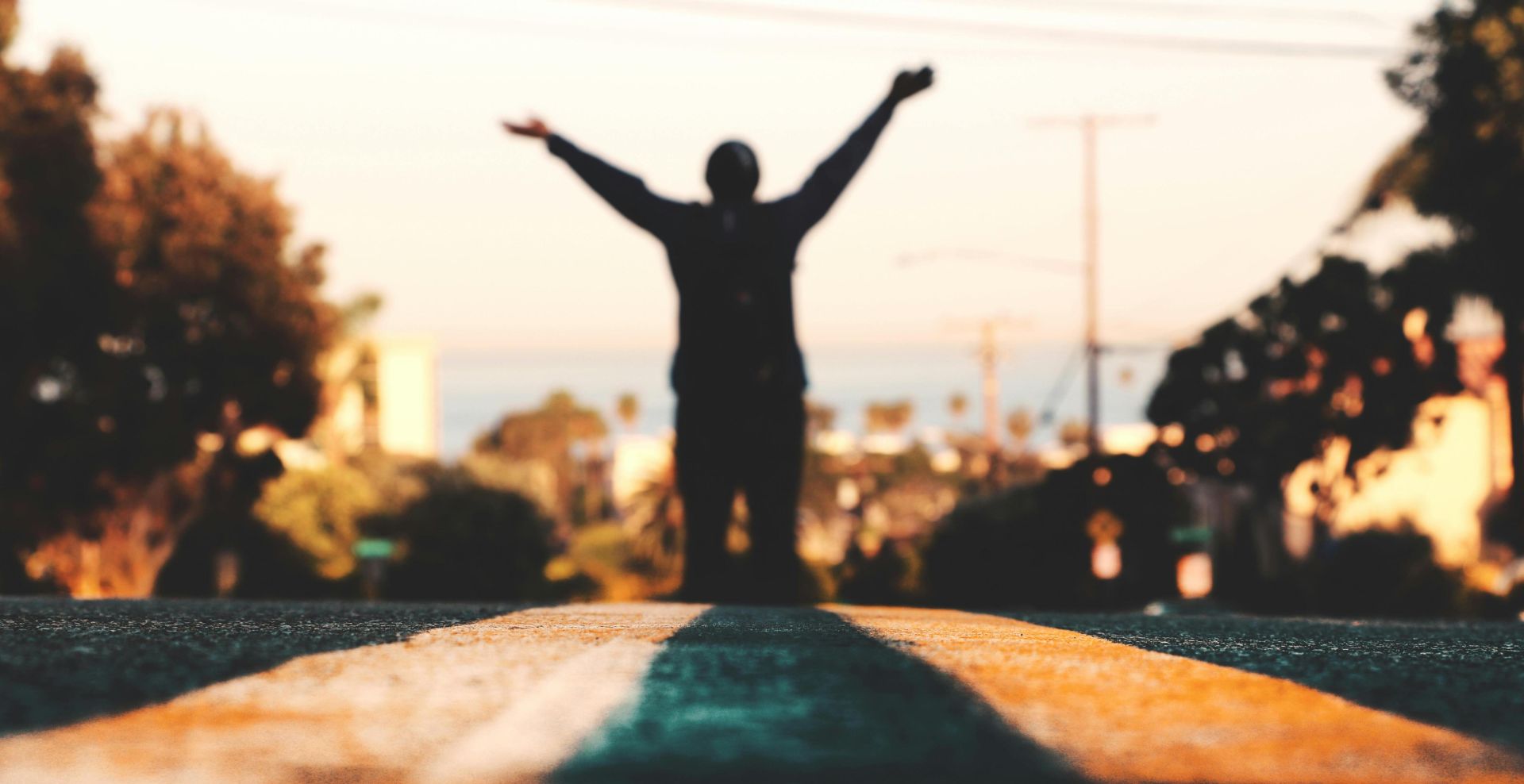 Silhouette of a person celebrating on a road during a vibrant sunset, creating a picturesque urban landscape.