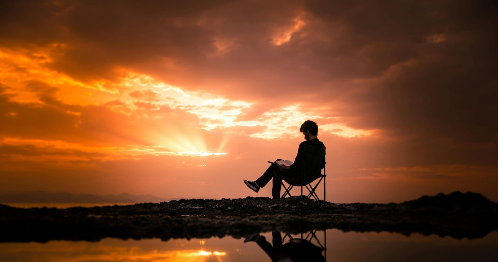 A person reading on a chair by a reflecting pond at sunset in Korgan, Turkey.