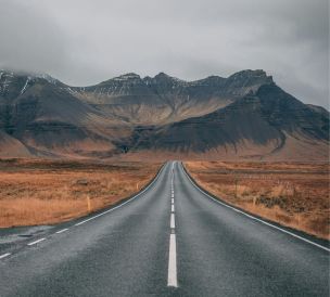 A scenic empty road stretches into snow-capped mountains under cloudy skies, offering a sense of adventure and tranquility.